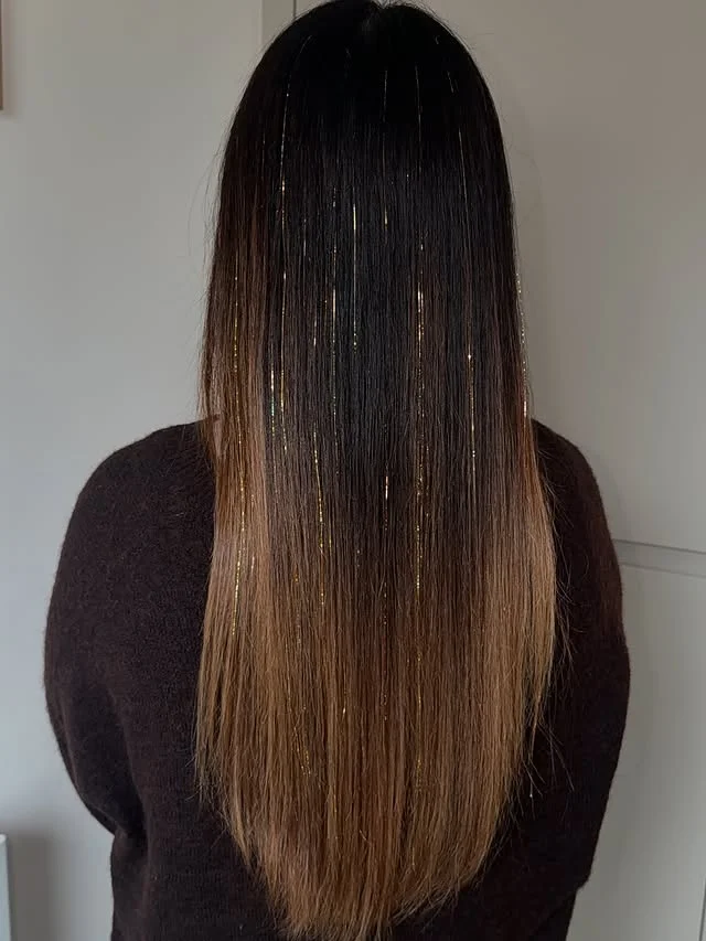 Back view of long straight ombre brown hair with thin gold tinsel strands woven through.