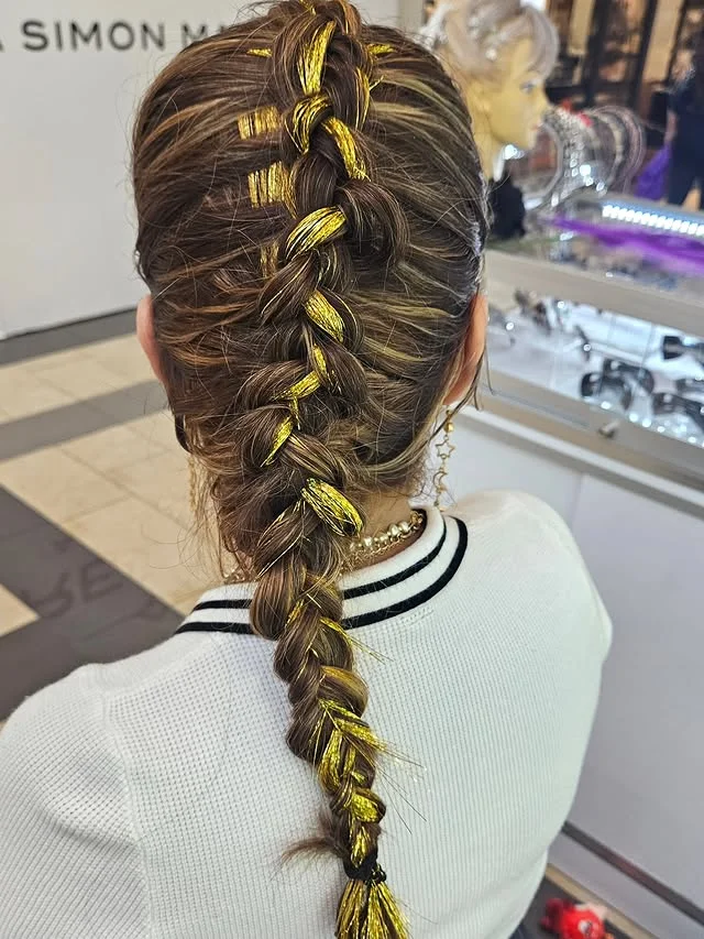 Back view of a long brown braid with gold metallic tinsel strands woven through the plaits.