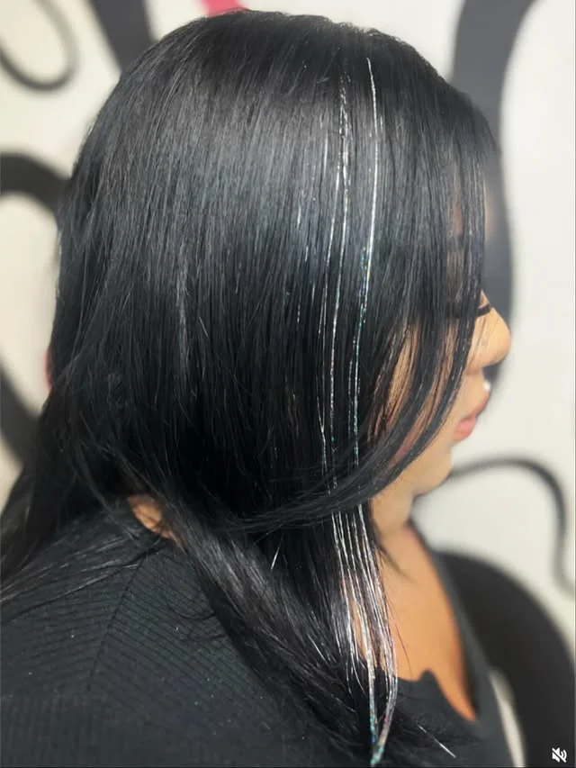 Side view of long dark hair with iridescent silver glitter strands threaded through.