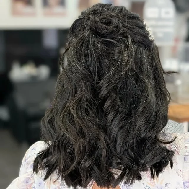Back view of a black wavy half-updo with subtle glitter particles and a small jeweled hair clip.