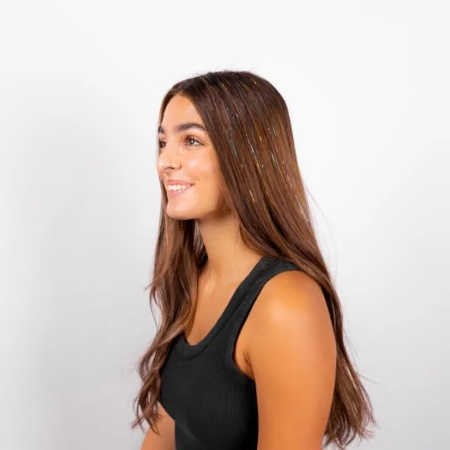 Studio portrait of a woman with long brown hair threaded with thin iridescent tinsel strands.