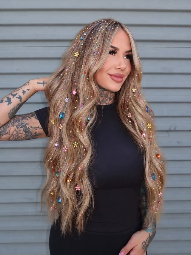 Woman with long wavy blonde hair covered in multicolored rhinestones and flower-shaped hair gems.