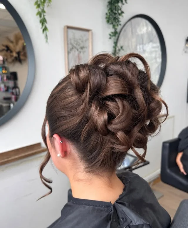 Brown updo with twisted sections, curls and volume with loose tendrils at the neck.