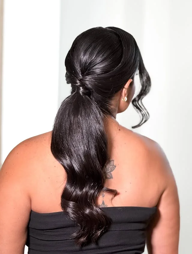 Sleek low ponytail with a twisted knot detail flowing into soft waves.