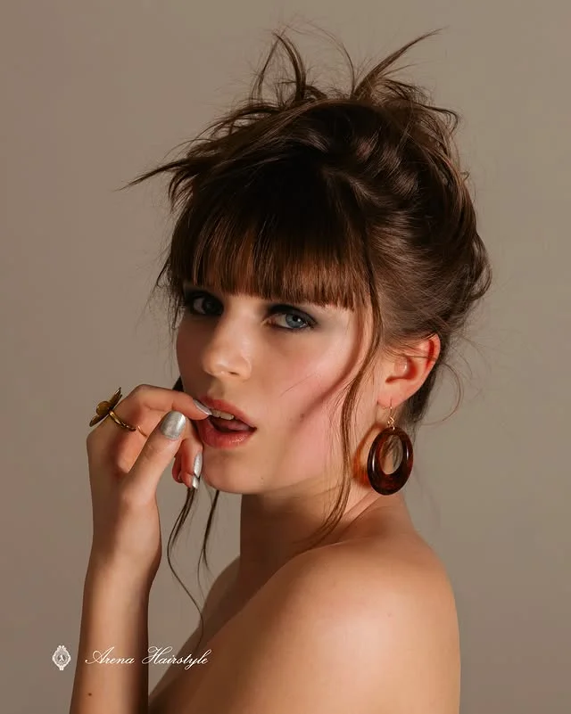 Front view of a voluminous textured updo with blunt bangs.